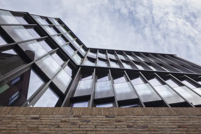 Upward view of the dark metal window grid cantilevering over the textured brick plinth