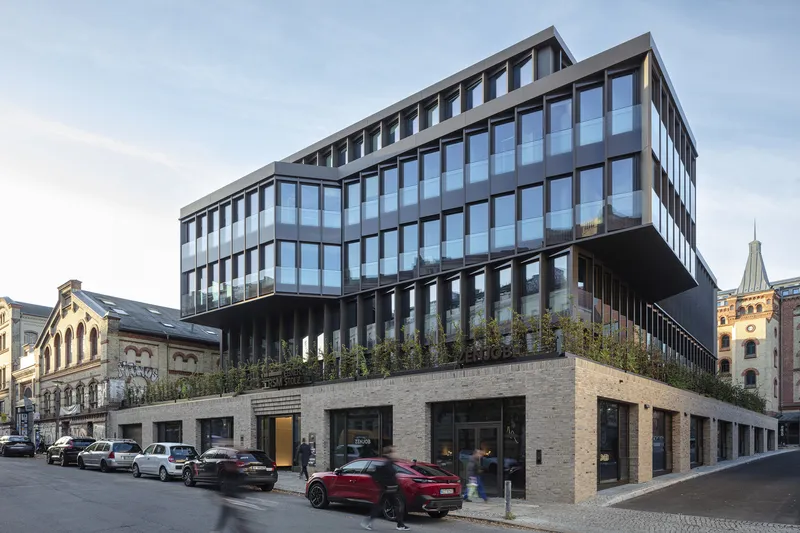 Corner facade with planted terrace band dividing brick base from dark-framed glass office floors
