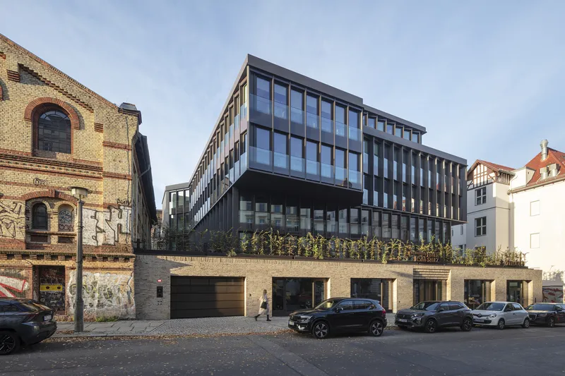 Street view of the dark glazed facade rising above a brick base with parked cars below