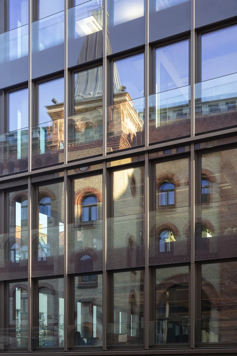 Glass curtain wall reflecting the arched windows of the adjacent brick warehouse in afternoon light
