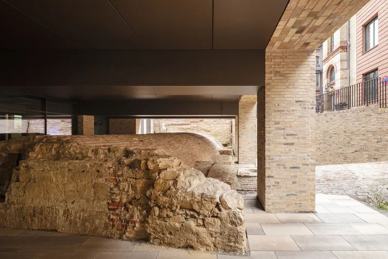 Covered passageway with exposed earth and stone foundation remnants beneath a smooth ceiling