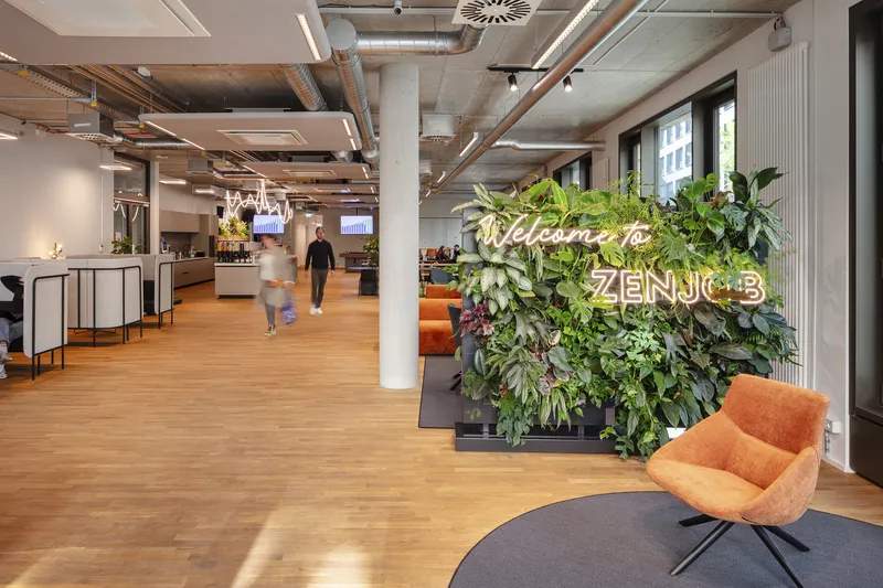 Open office space with exposed concrete ceiling beams and a vertical planted wall near the entrance