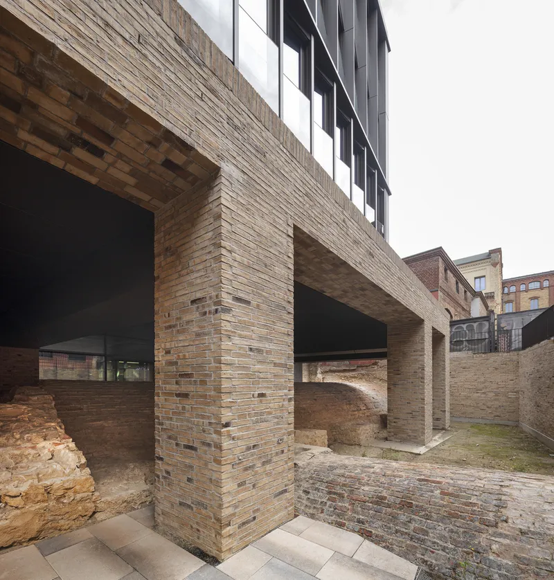 Brick piers supporting the elevated volume above excavated archaeological ruins and cobblestone paving