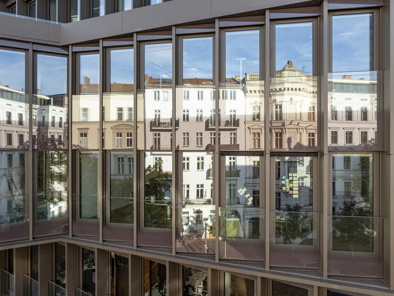 Floor-to-ceiling glazed facade reflecting surrounding residential buildings and a tree-lined courtyard below