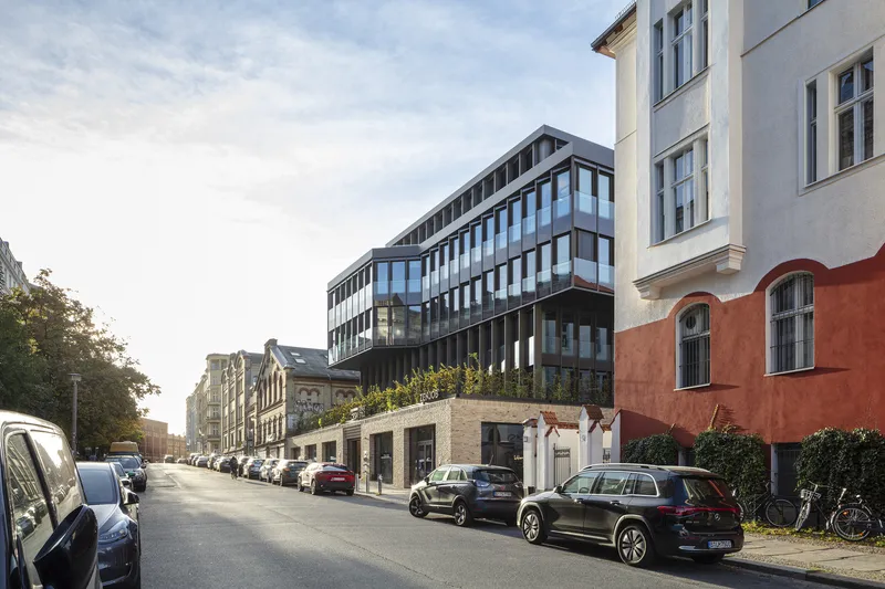 Street view of the dark facade with horizontal window bands rising above a brick base and parked cars
