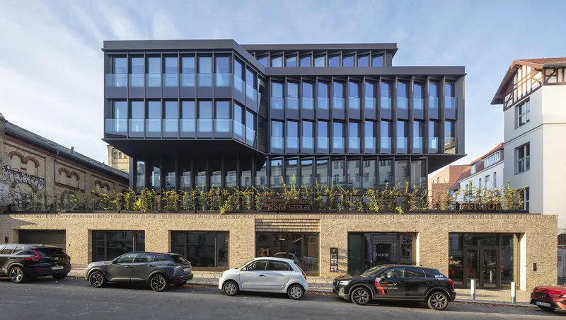 Front elevation showing cantilevered upper floors above a brick plinth with planted terrace and shopfronts