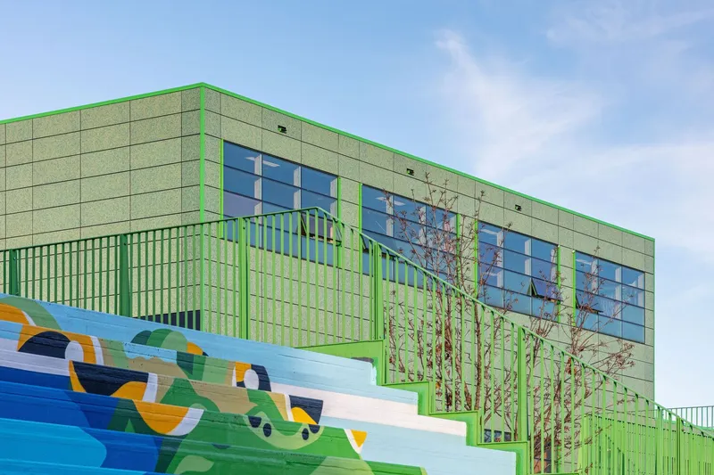 Detail of green metal railing and paneled facade above painted mural with young planted trees