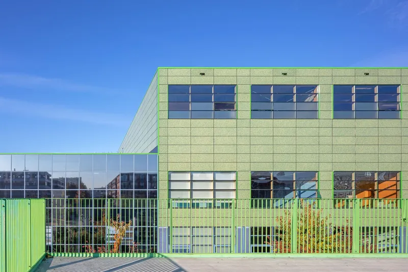 Lime green panel facade with horizontal window bands and vertical metal screening behind young trees