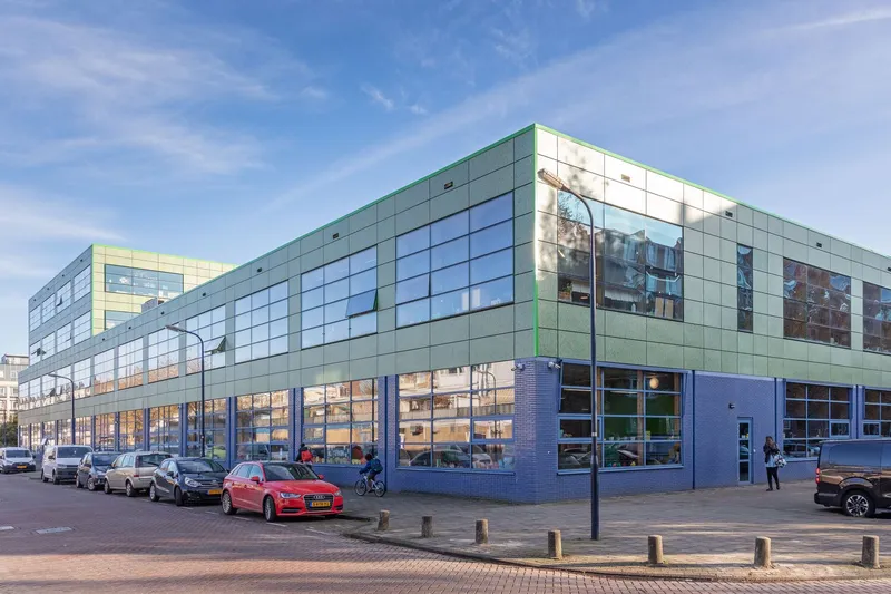 Corner view of the green paneled building with glazed ground floor and parked cars at dusk