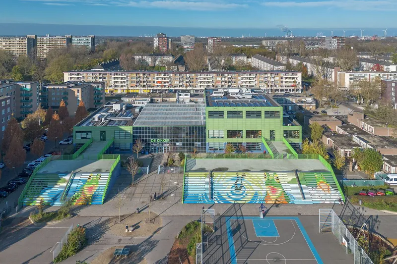 Aerial view of the green school building with rooftop solar panels and painted sport courts below