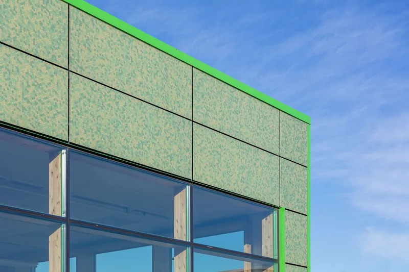 Corner detail of the green-trimmed facade with textured panels above dark-framed glazing