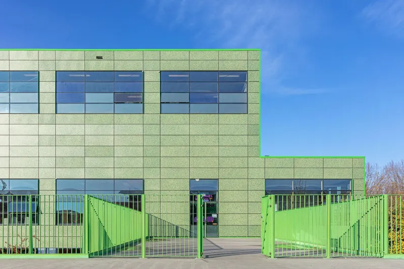 Textured green panel facade with ribbon windows and open metal gates under a clear blue sky