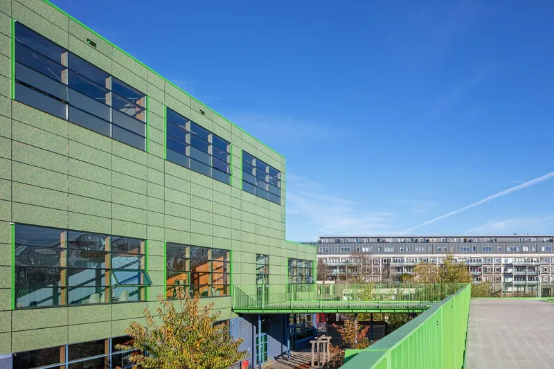 Exterior view showing the green panel building with an elevated walkway and distant residential block