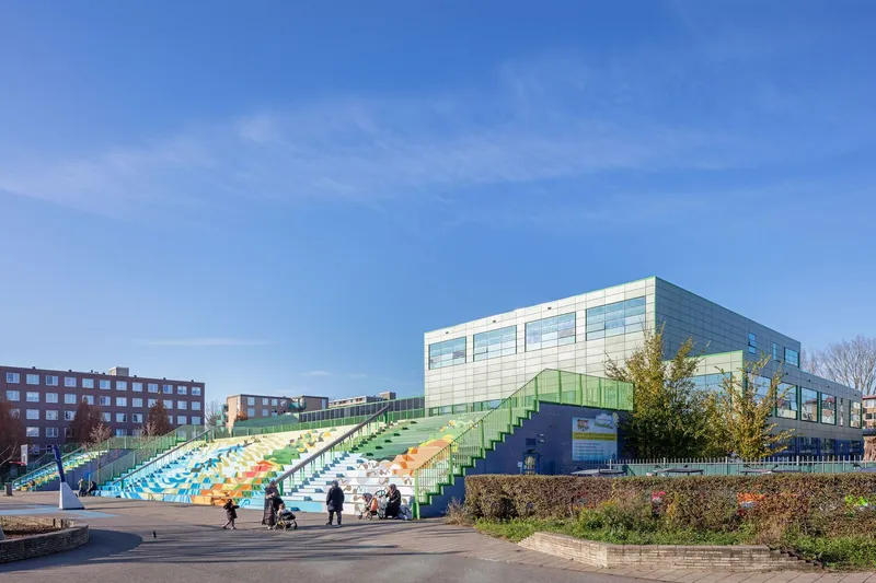 Terraced seating with multicolored stripes stepping up to the green paneled facade under a clear blue sky