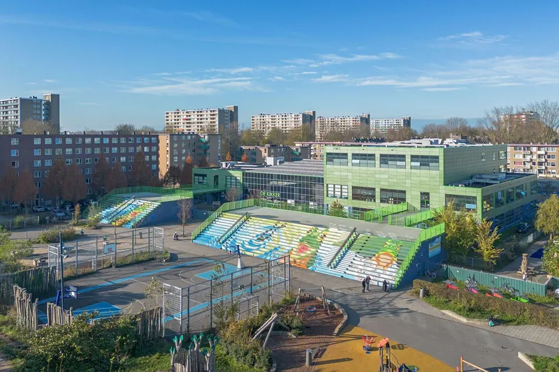 Elevated view showing the terraced seating leading to the paneled facade with a playground in the foreground
