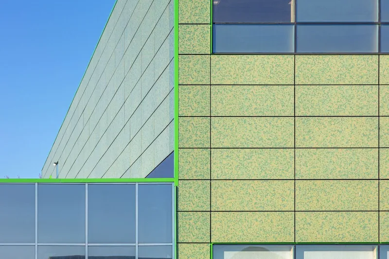 Corner detail of the facade showing green panel joints and window mullions against a clear sky