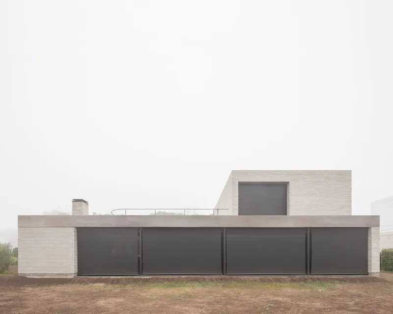 Street facade: opaque two-metre wall with dark steel panels, rooftop terrace above
