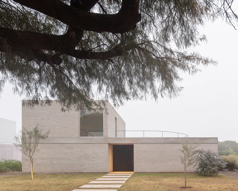 Garden approach: the two-storey brick volume framed by a mature tree, overcast sky