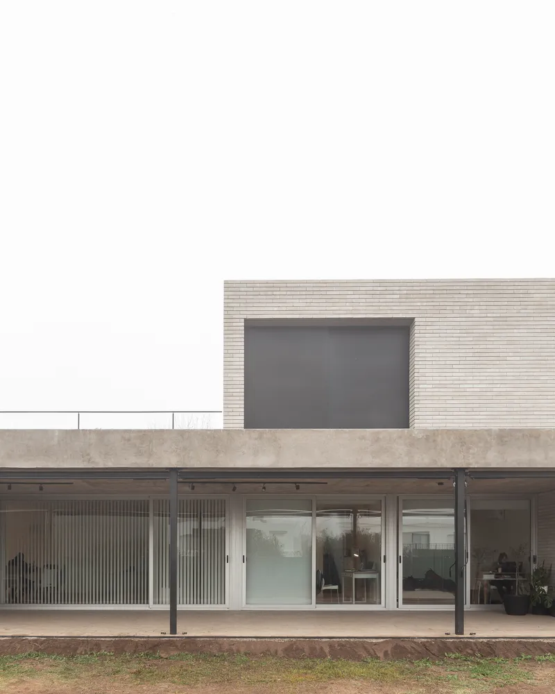 Garden elevation: ground-floor glass wall open to the backyard, upper brick volume set back