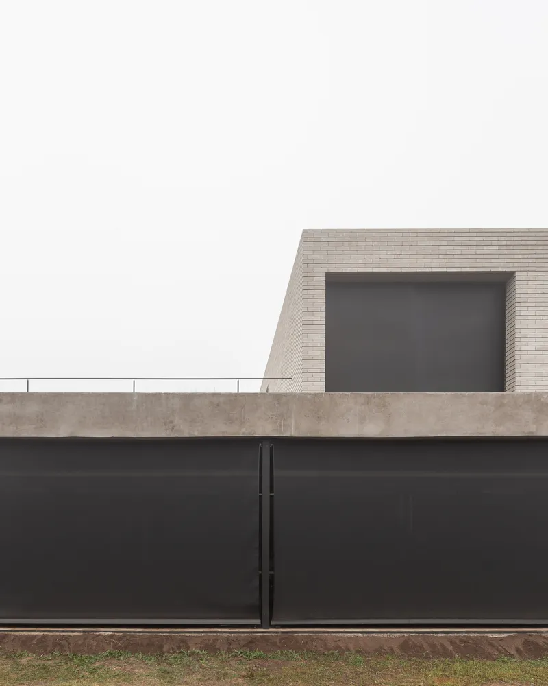 Street boundary: dark steel wall and gate with brick volume and window rising above