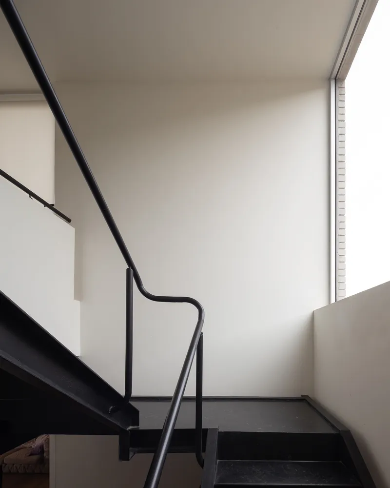 Stair detail: black steel stringer and handrail, white walls, clerestory window above