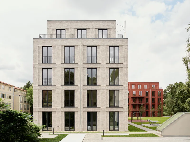 Five-story pale brick facade with floor-to-ceiling windows facing a grassed courtyard under an overcast sky