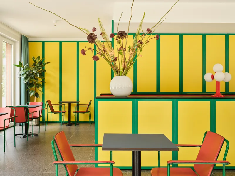 Common room with yellow paneled wall framed in green and a vase of dried branches on the half-height divider