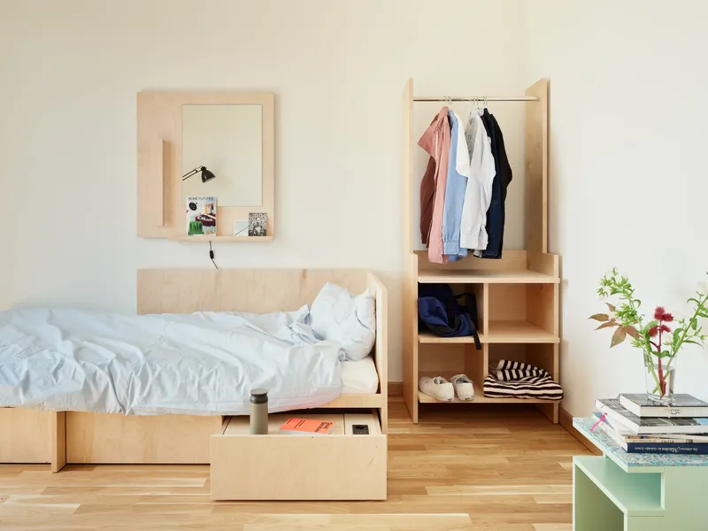 Bedroom with light wood platform bed, open wardrobe unit and clothing hanging on a rail