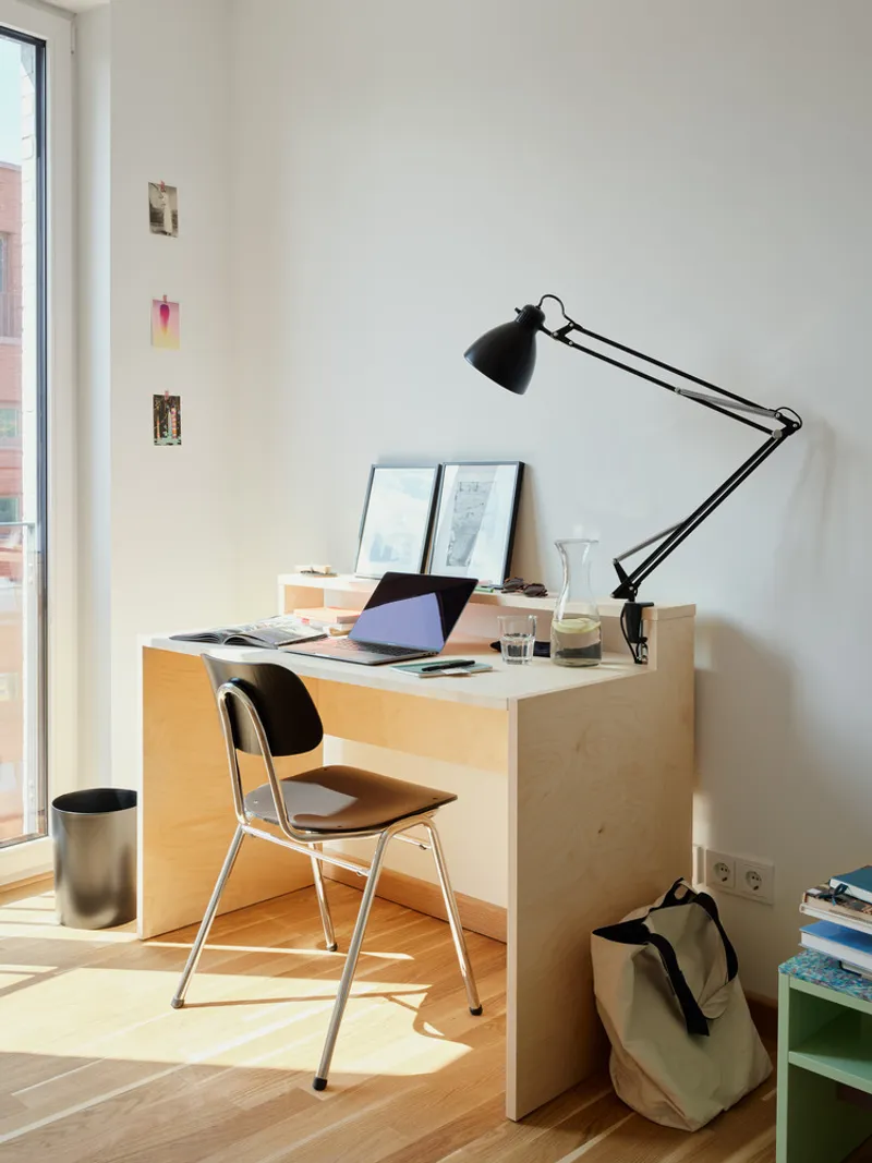 Workspace with plywood desk, articulated task lamp and afternoon sunlight on oak flooring