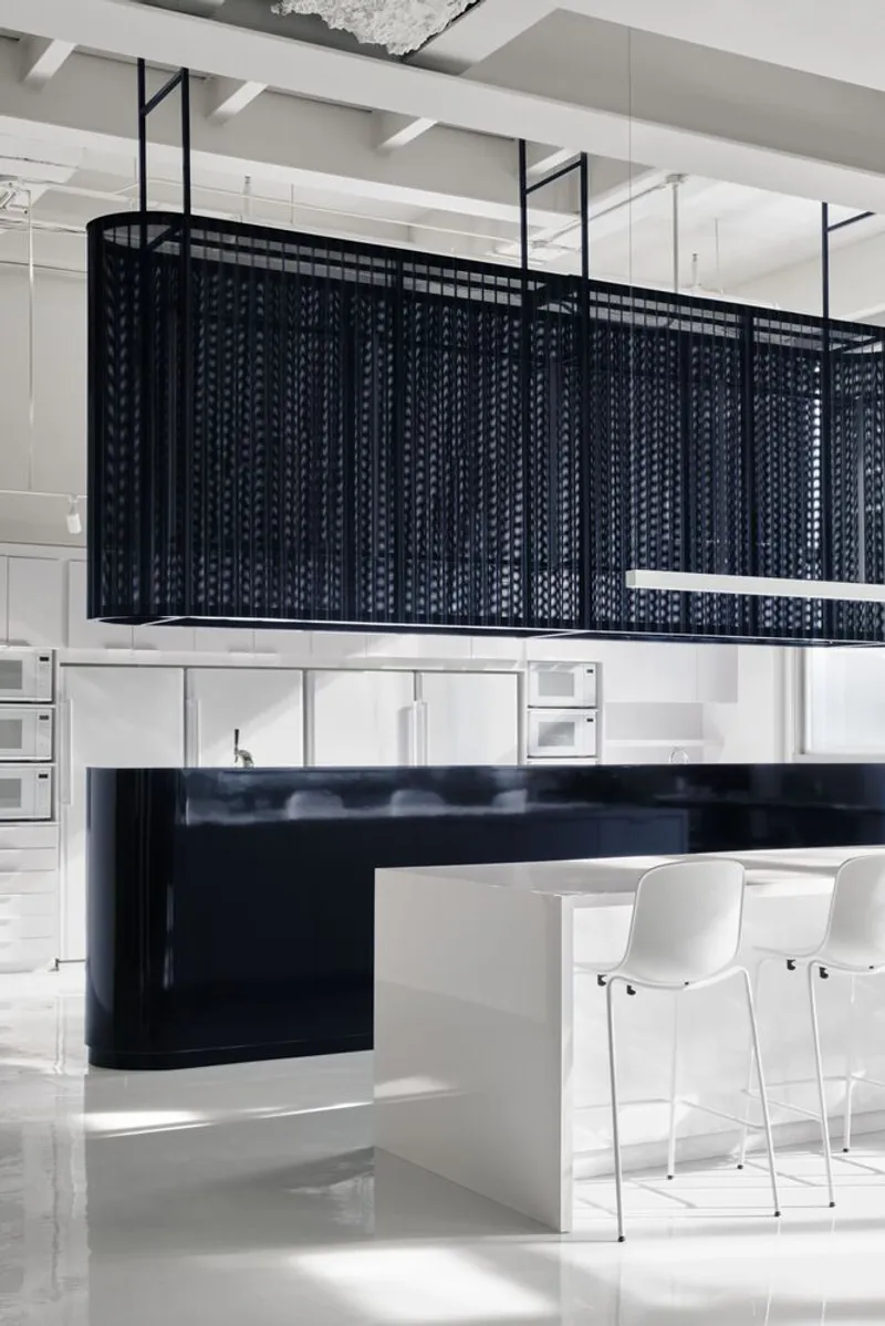 Kitchen island with suspended black perforated metal screen and white counter stools in daylight