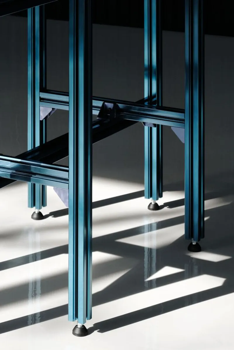 Close-up of blue anodized aluminum table base with adjustable feet on reflective white floor