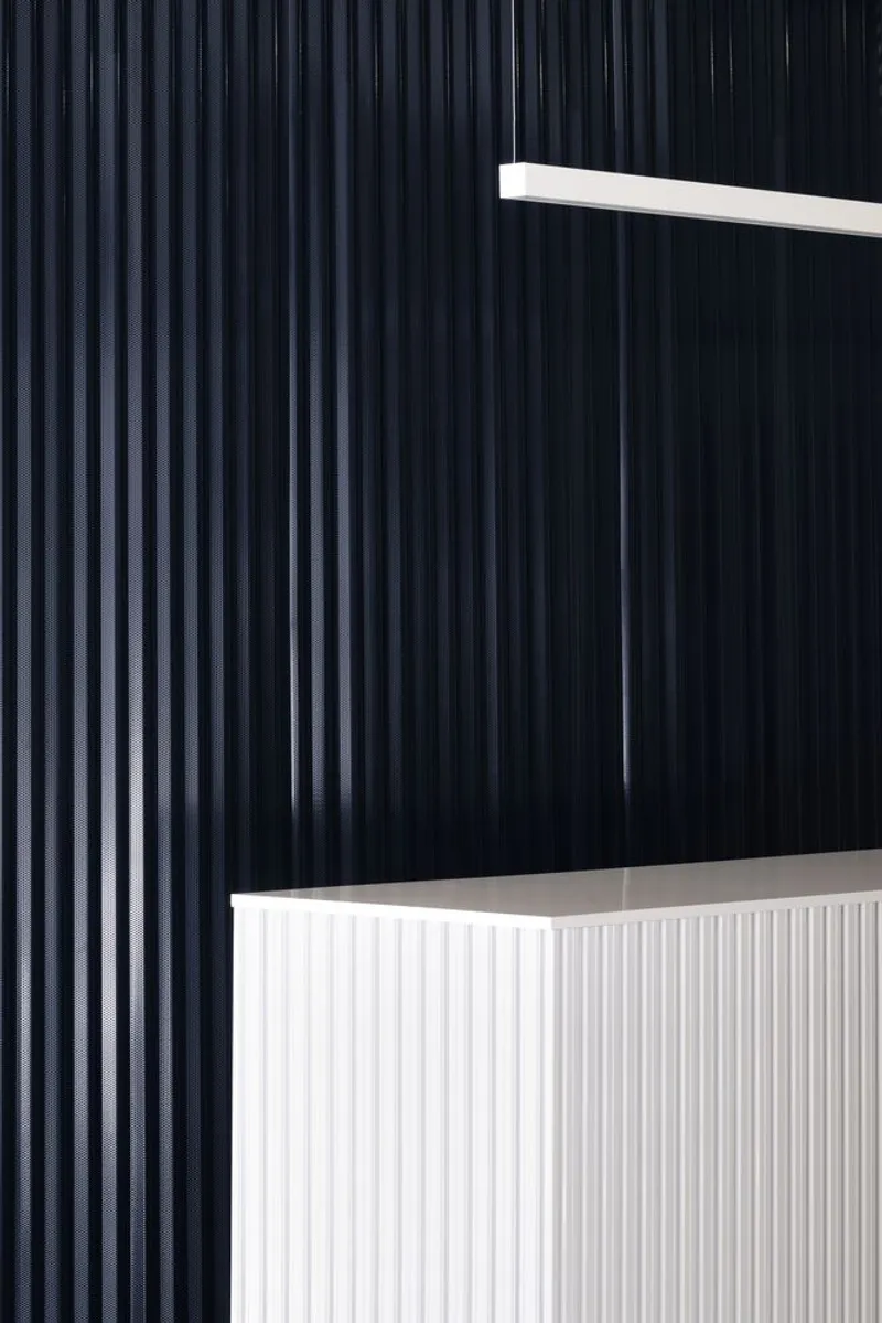 Vertical corrugated black wall panel beside white reception counter with linear lighting above