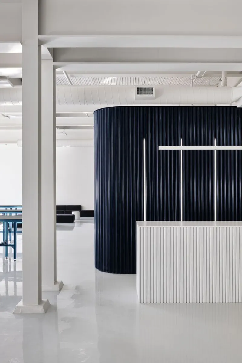 Reception counter with vertical white slats beside a curved wall clad in dark ribbed panels
