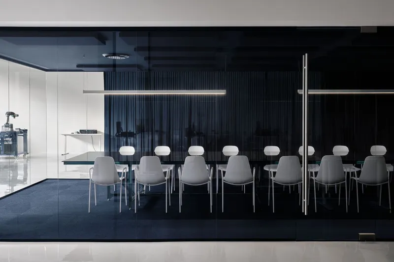 Conference table with grey upholstered chairs arranged in rows before a dark ribbed acoustic wall