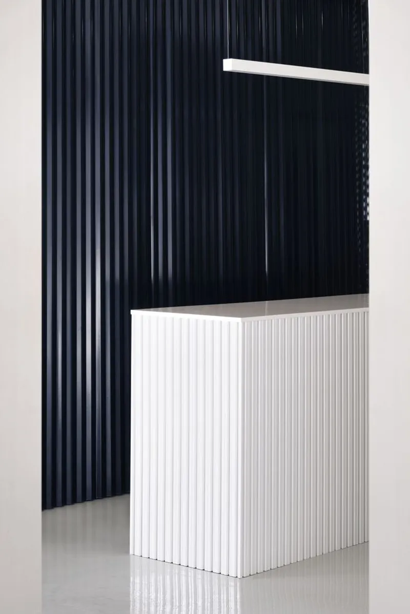 Detail of a white vertical-slat counter base against a dark ribbed curved wall panel