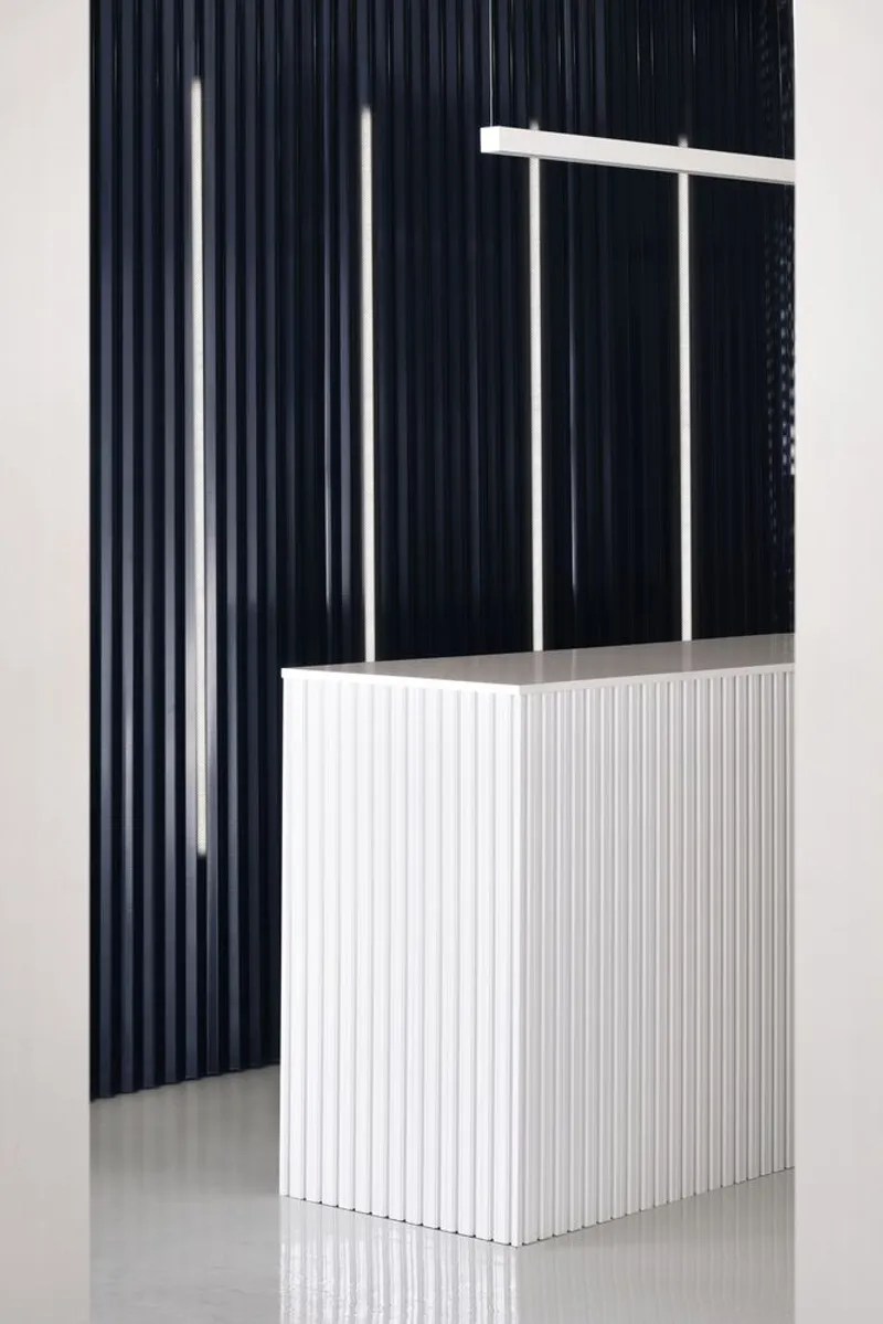 Reception desk with vertical white ribbed cladding against a dark blue corrugated wall with suspended linear lighting
