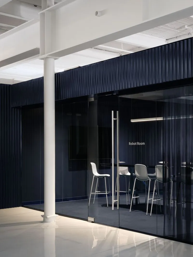 Glass enclosed room with high stools against dark blue fluted wall and white structural columns