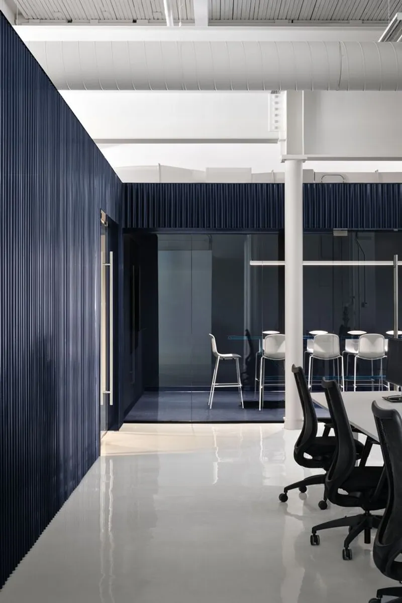 Open office workstations with dark blue ribbed enclosure and glazed meeting room under industrial ceiling