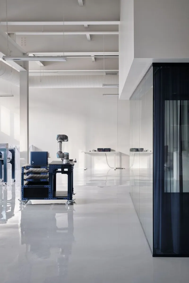White interior with exposed beam ceiling, polished floor, workstation cart and glass-fronted dark volume