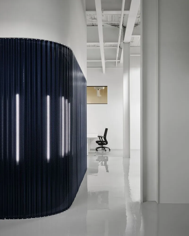 Blue perforated curved screen with integrated vertical lights next to white columns and exposed ceiling structure