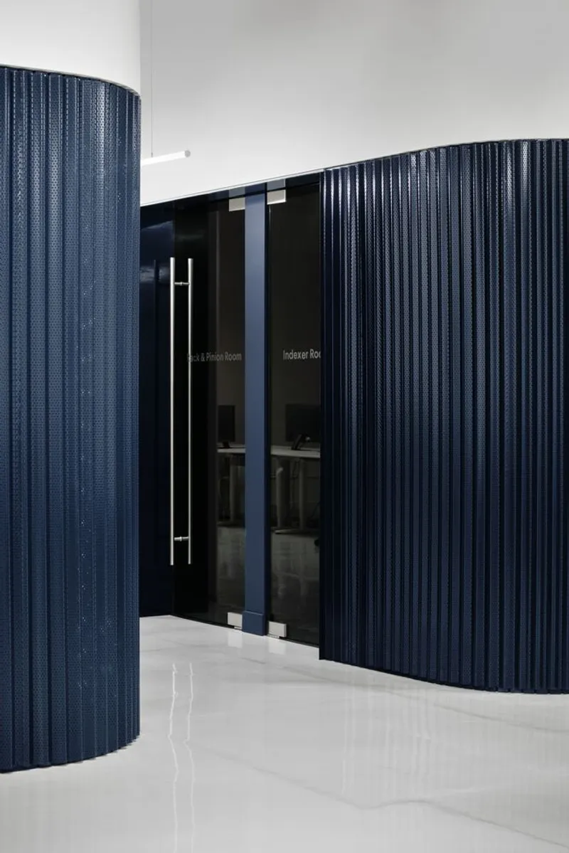 Curved dark blue fluted partition walls with glass doors and vertical handle under white ceiling