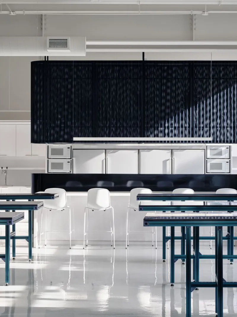 Communal dining area with suspended black mesh partitions above white kitchen island and reflective floor