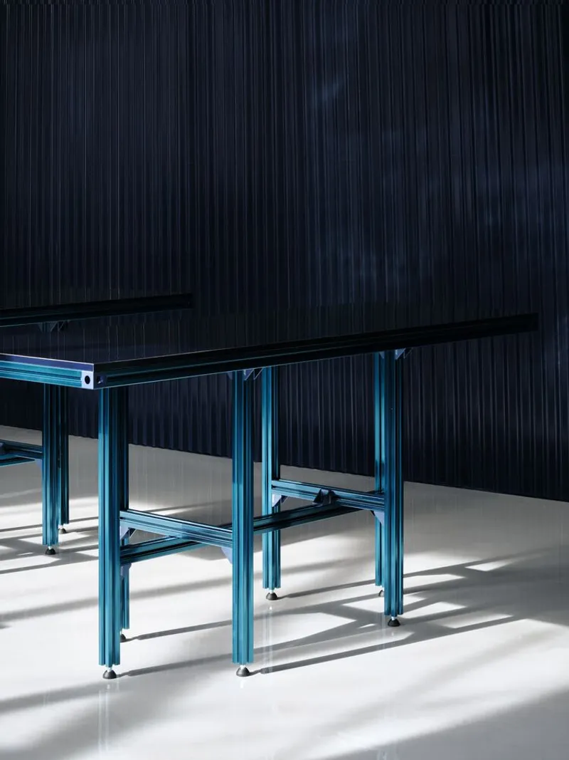 Blue tubular steel table legs casting shadows on polished floor near dark corrugated wall