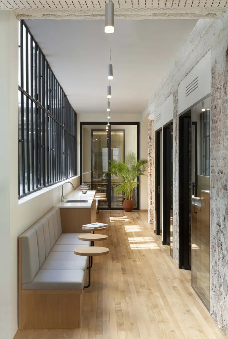 Narrow corridor with banquette seating: oak floor, steel-frame windows, pendant lights, pink cushions
