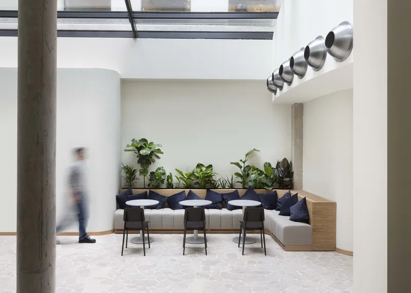 Courtyard lounge: glass roof overhead, concrete columns, built-in bench with plants, spherical chrome light fixtures