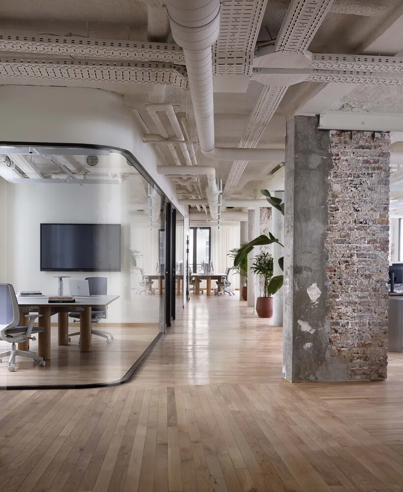 Open office floor: exposed brick column, concrete column, oak floors, exposed ductwork, plants, modern workstations