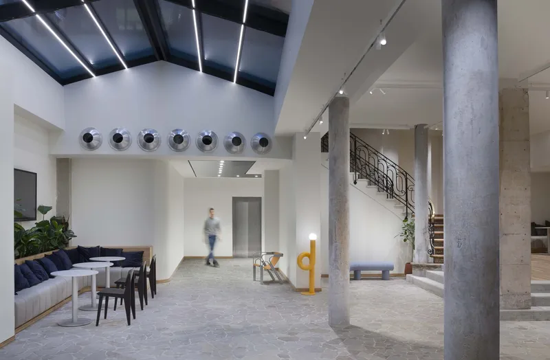 After: courtyard ground floor with glass roof, concrete columns, iron staircase, lounge seating, chrome spheres