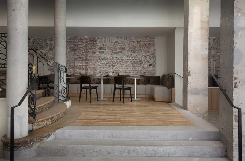 After: ground floor lobby with restored iron staircase, exposed stone columns, brick wall, oak-floored raised seating area