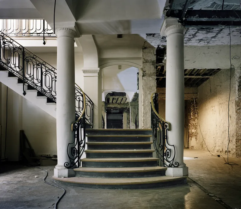 Before: grand entrance staircase with columns, iron railings, worn stone, exposed wiring