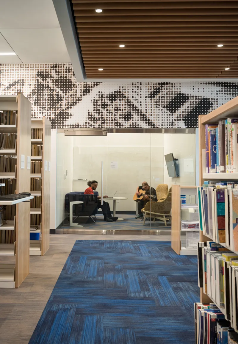 Reading alcove beneath perforated metal mural and timber slat ceiling with two patrons seated inside